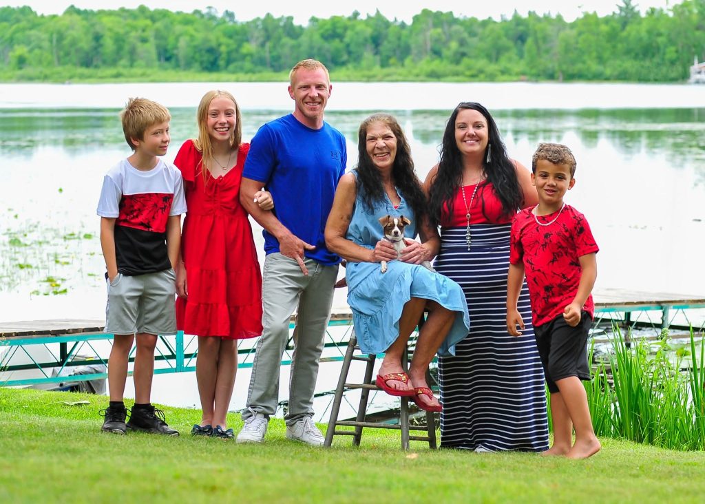 Family of six laughing together on a lakeshore lawn