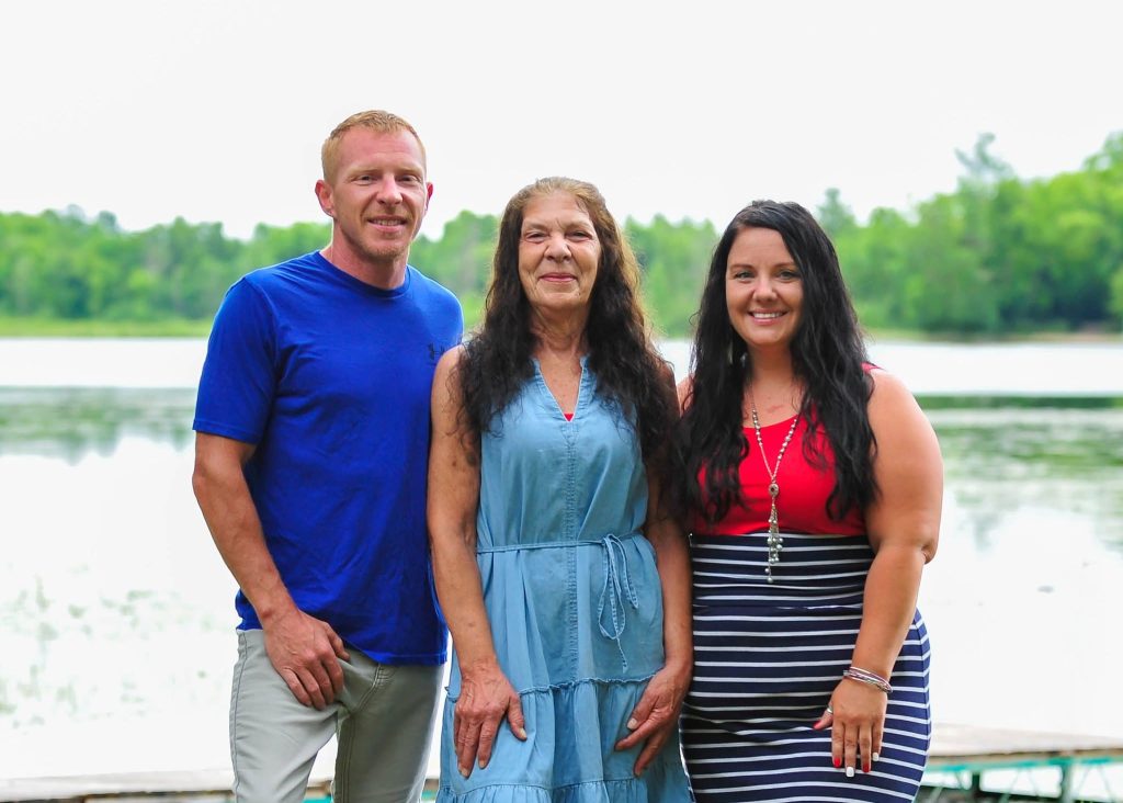 Three adults standing together on a lakeshore