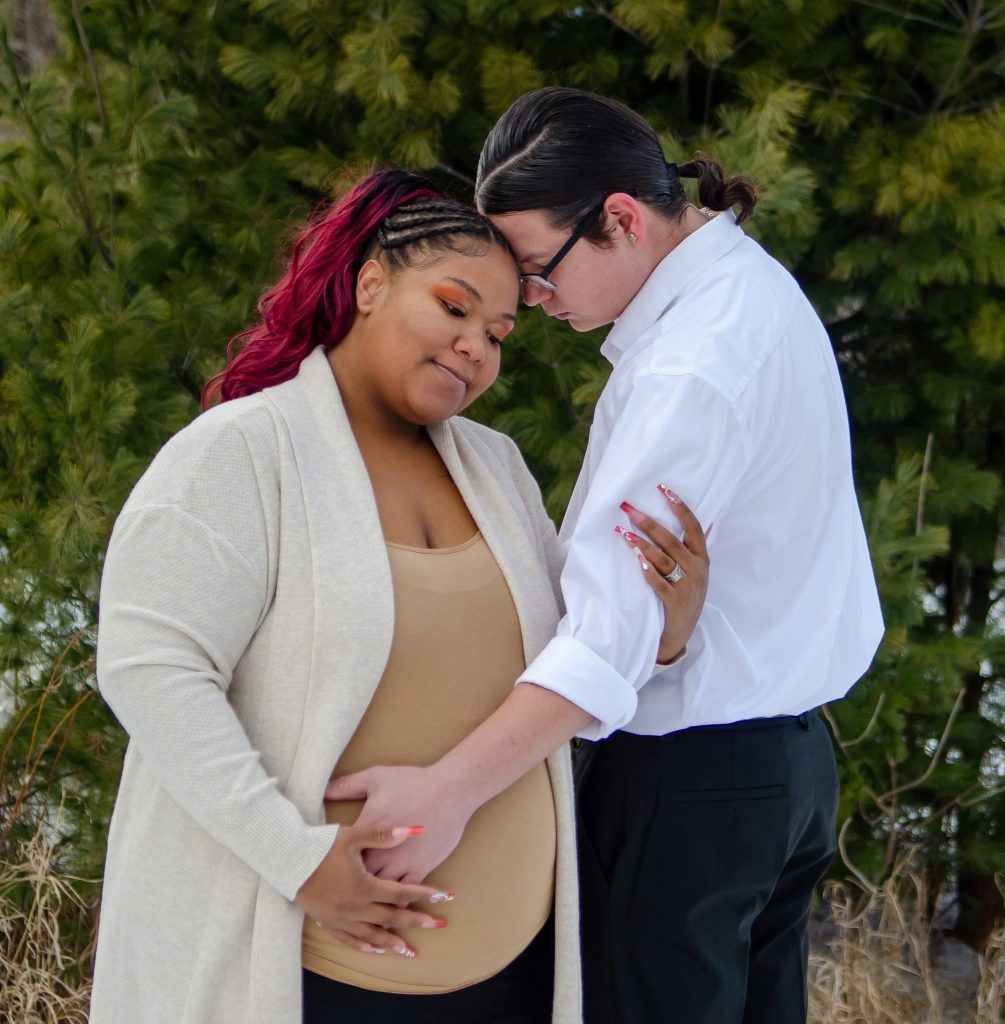 Expecting couple forehead to forehead among evergreens
