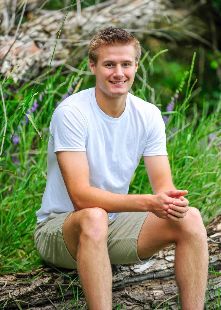 Senior portrait of a young man seated on a log in tall grass
