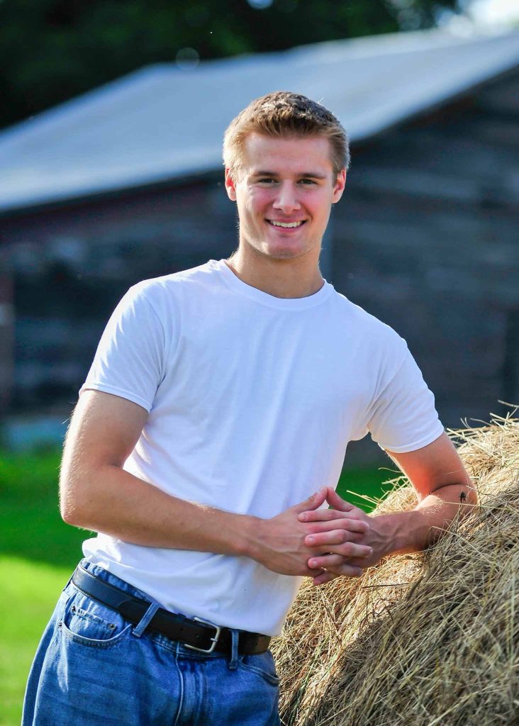 Senior portrait leaning on a hay bale by a barn