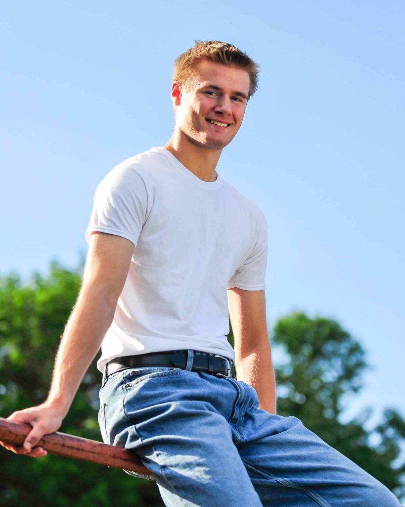 Senior sitting on a fence rail under a blue sky