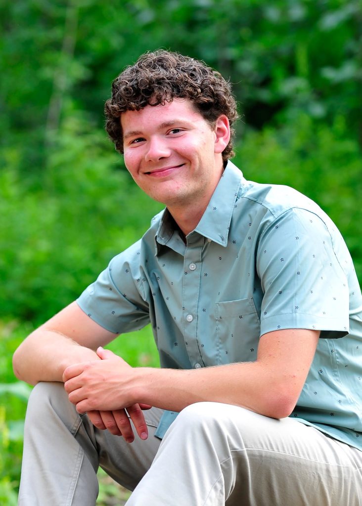 Senior portrait crouching in summer greenery