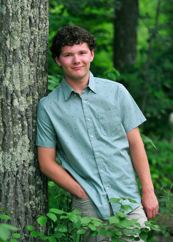 Senior leaning against a tree in the woods